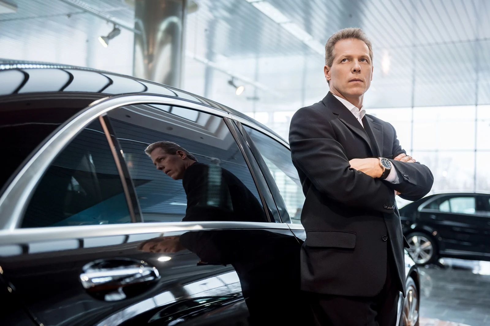 Professional chauffeur standing beside a black luxury sedan