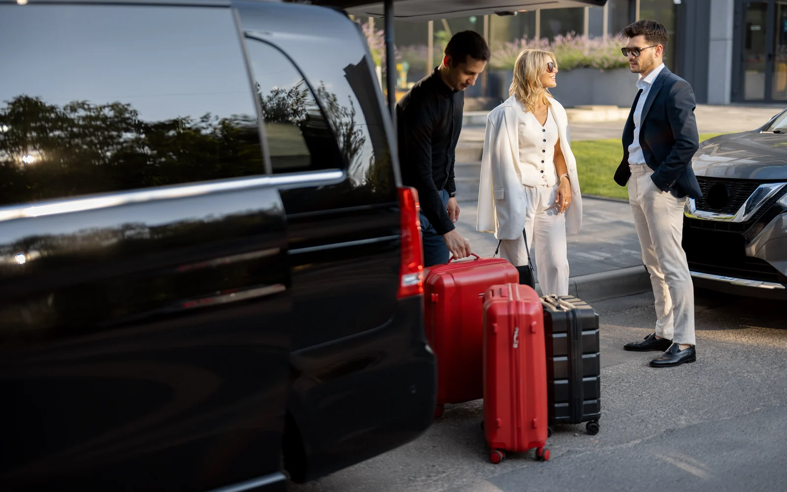 Chauffeur assisting passengers with luggage beside a luxury vehicle for an airport transfer