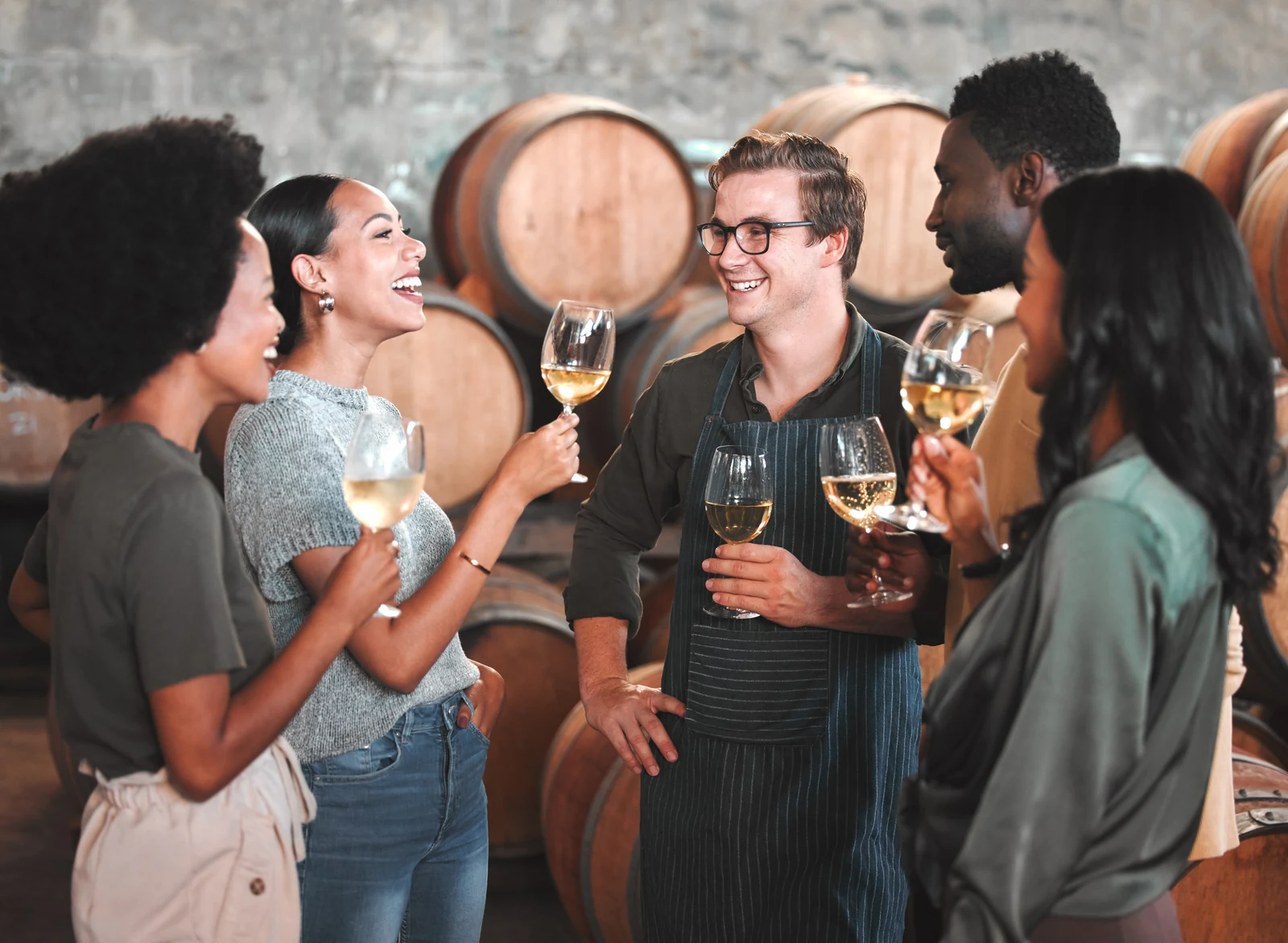 Winemaker sharing white wine with guests in a barrel room